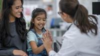 kid seated next to mom high fiving doctor